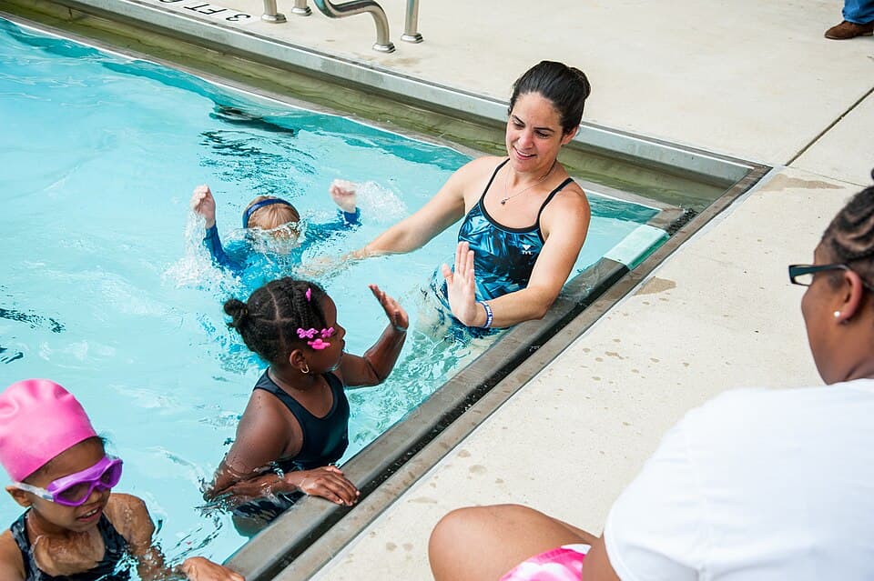 Children learning to swim and exchanging a high five with an instructor