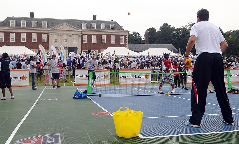 Children practicing tennis with a coach on a small court